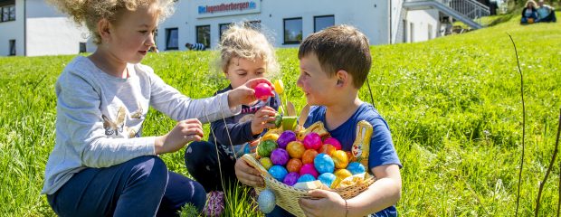 Drei Kinder sammeln bunte Ostereier vor der Jugendherberge Tholey