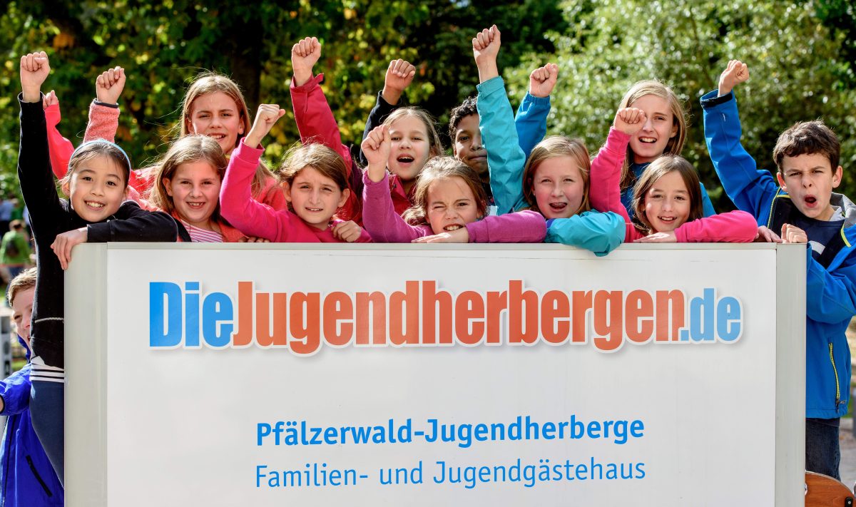 Eine Schulklasse steht hinter dem Schild der Jugendherberge und jubelt