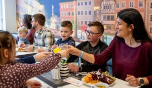 Eine Familie im Restaurant der Jugendherberge Trier. Die Mutter sitzt mit den Kindern am Tisch. Sie stoßen mit gefüllten Gläsern an.