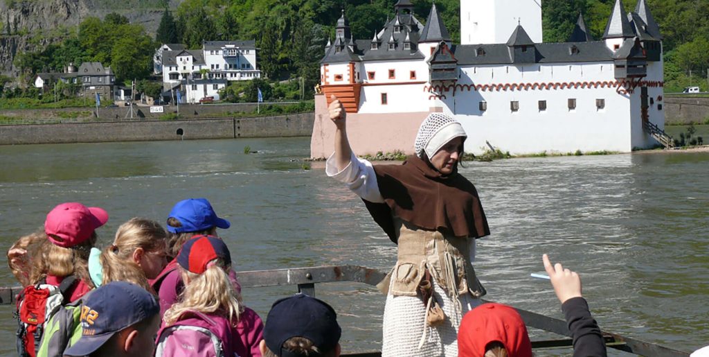 Eine als mittelalterliche Magd verkleidete Führerin erklärt einer Gruppe von Schulkindern die Burg Pfalzgrafenstein im Rhein.