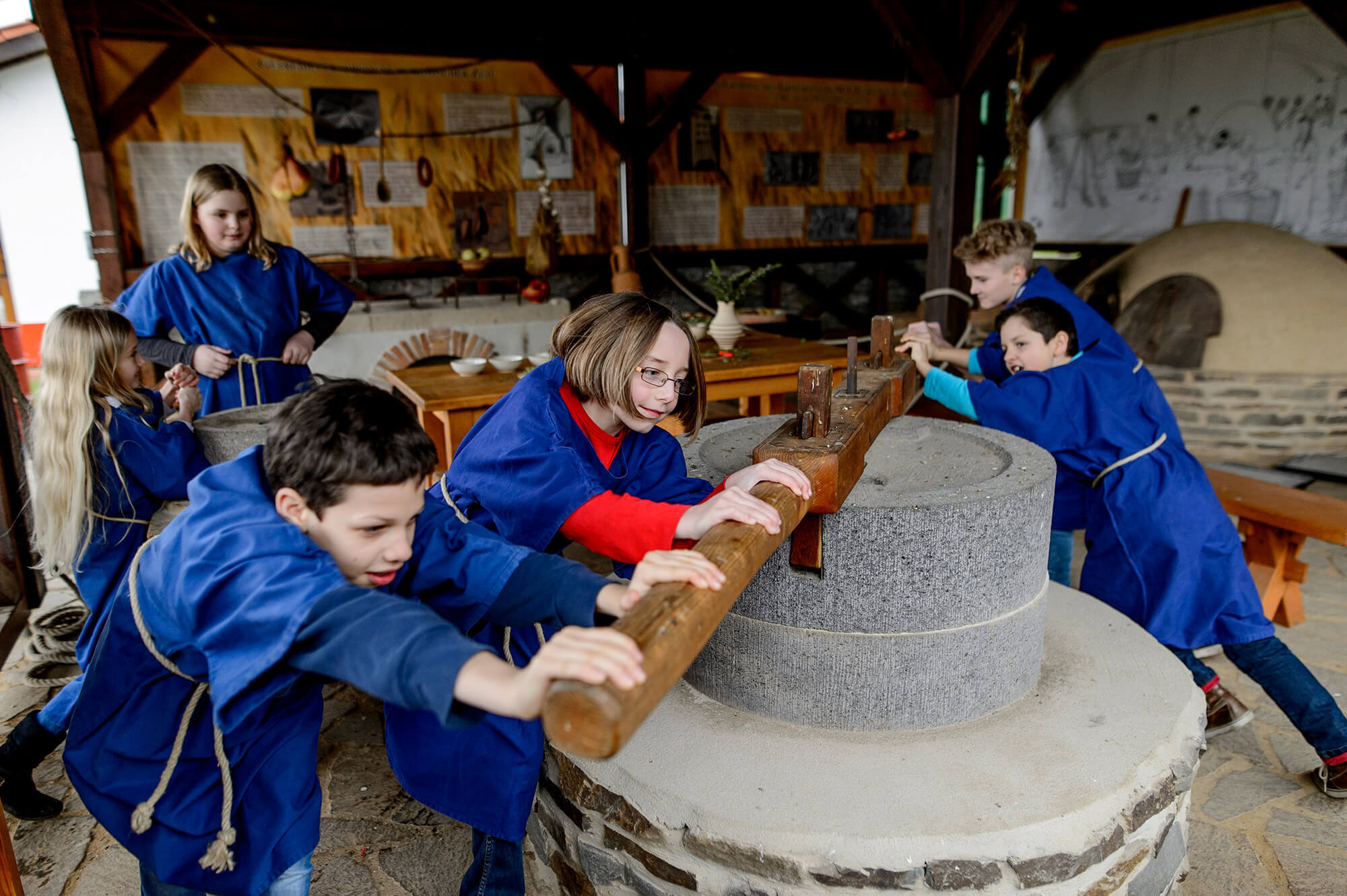Neuzeit entdecken: Schüler in blauen Tuniken bedienen gemeinsam eine historische Steinmühle zum Mahlen von Getreide.