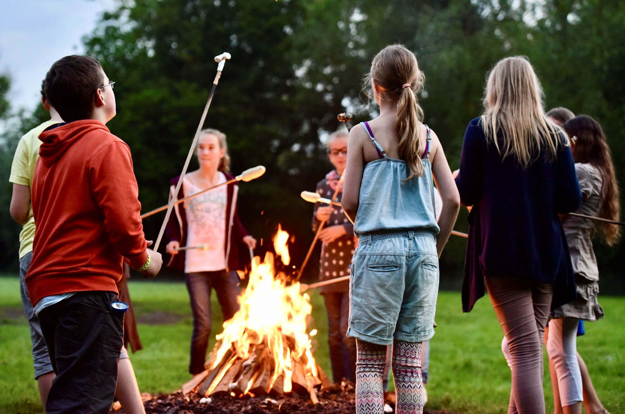 Schülergruppe röstet gemeinsam Stockbrot über einem Lagerfeuer – ein stimmungsvoller Abend während einer Klassenfahrt.