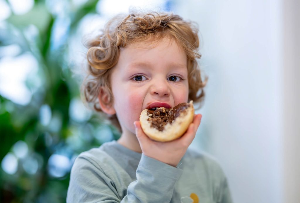 Ein Junge beißt genussvoll in ein Brötchen mit Nuss-Nougat-Creme